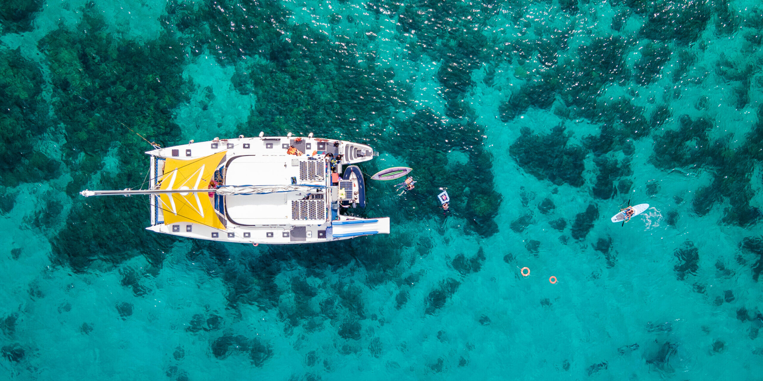 Aerial top view of sailing catamaran anchor over turquoise water with tourists swimming and paddle boarding at Racha Yai Island, A popular destination for summer vacation in Phuket, Thailand.